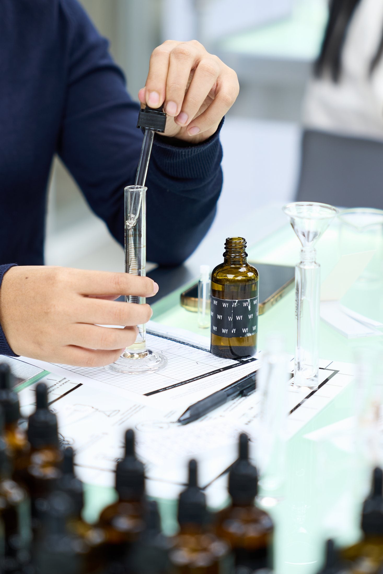 A hand uses a glass pipette to blend perfume at the fragrance-making bench.